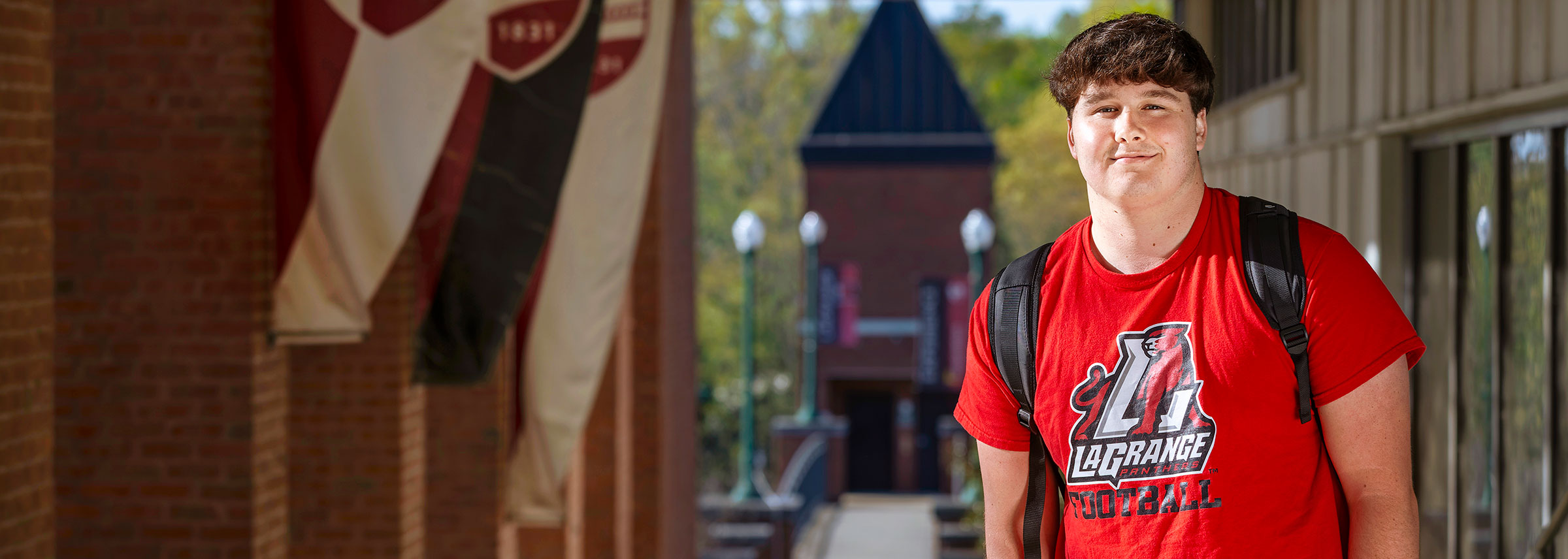 A male student in a red shirt stands at the top of the stairs that lead to the Gulley Gateway bridge