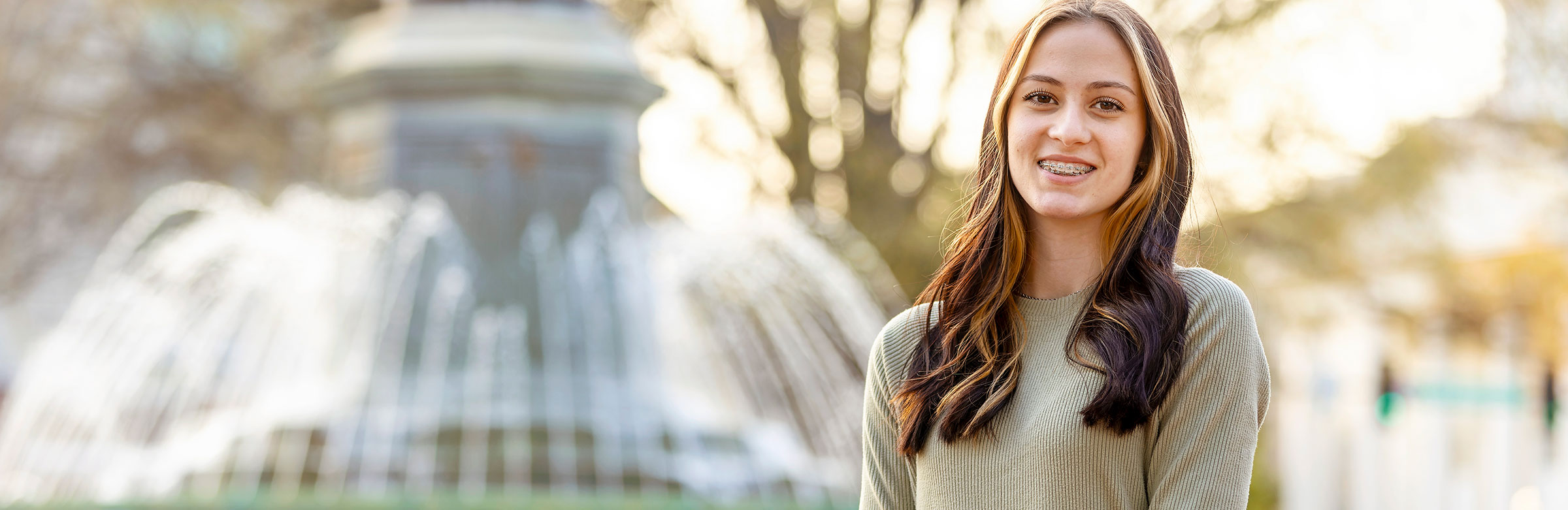 a smiling female student stands in front of a water fountain