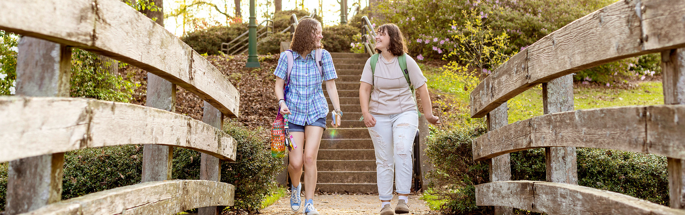 Two students walk across a wooden bridge on a sunny day