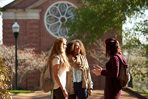 Three female student stand in front of the chapel talking