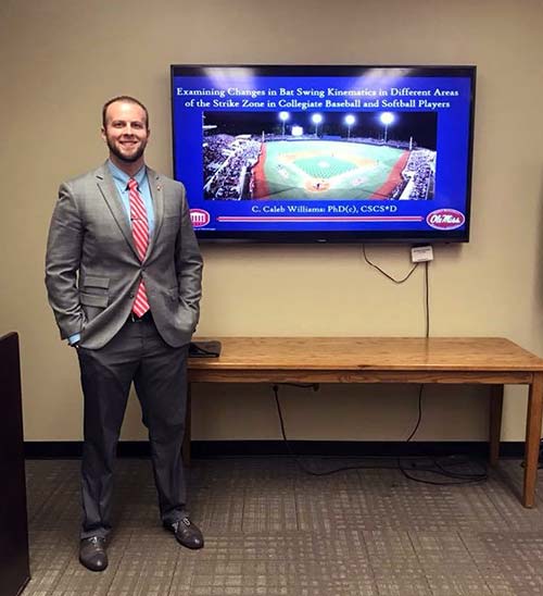 Professor Caleb Williams stands with a television depicting a Moroccan soccer game