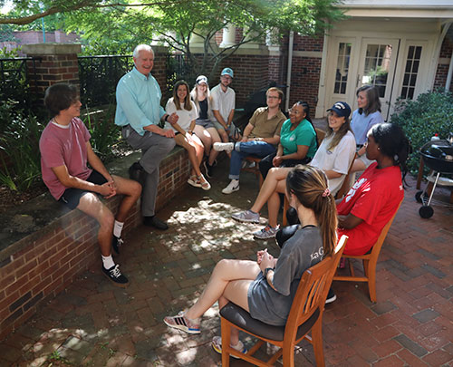 {A professor speaks to a group of students outside on a patio}