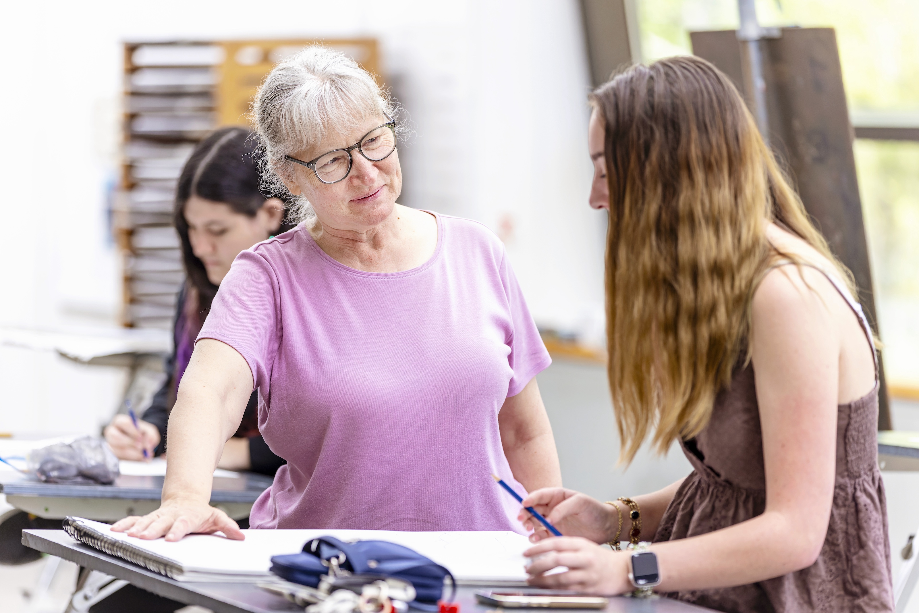 A professor explains drawing techniques to a seated female student.