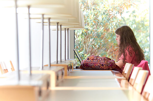 A woman sits at a long table working on a laptop