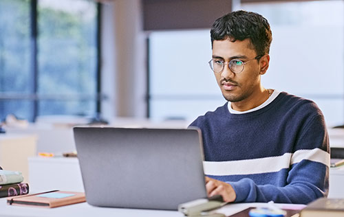 A male student studies on a laptop in a sunny room