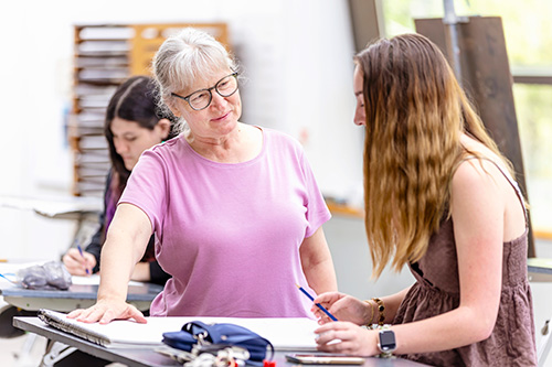 A professor instructs a drawing student at a sketch table