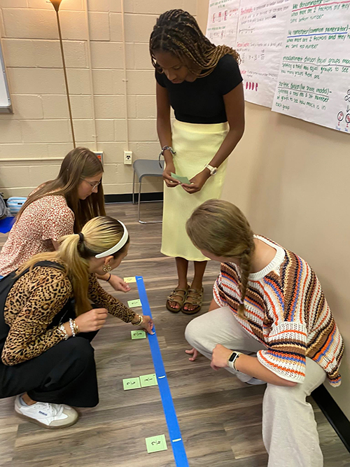 Four education students create a measurement exercise on the floor in preparation for teaching a class