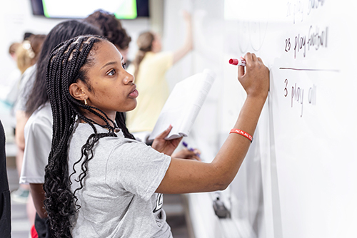 A female student works a math problem at a whiteboard