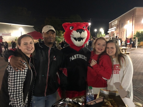 Four people stand with Pouncer at an evening alumni event