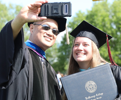 A student and professor take a selfie after a graduation ceremony